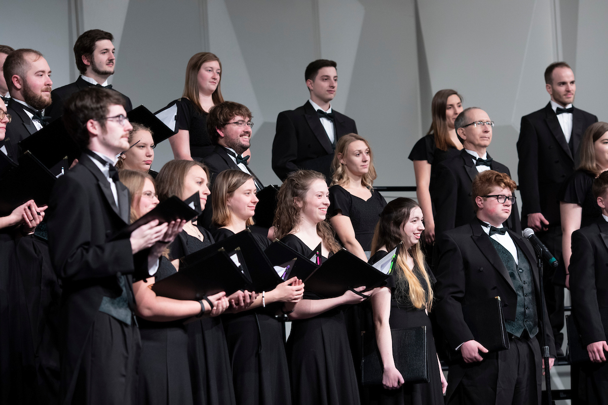 A choir dressed in formal black attire performs with sheet music in hand.